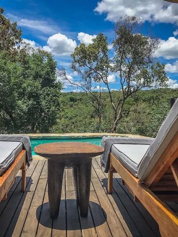 Holzterrasse mit zwei Liegestühlen und Blick auf den Pool und Bäume