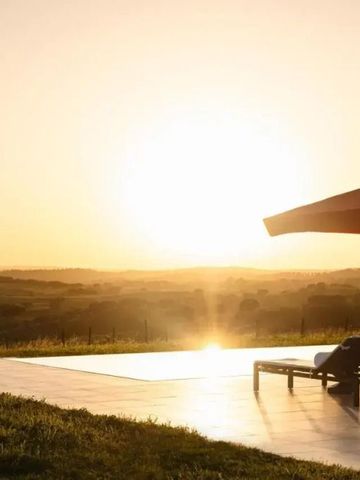 Sonnenuntergang über einem Außenpool mit Liegestühlen und Sonnenschirm