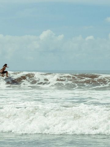 Surfer gleitet auf kraftvoller Welle unter strahlendem Himmel