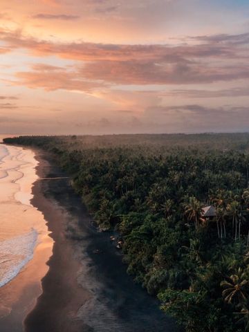Sonnenuntergang über tropischer Küste mit üppigem Regenwald und sanften Wellen