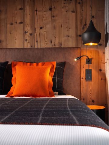 Detailansicht eines Betts mit orangefarbenen Kissen und Holzwand