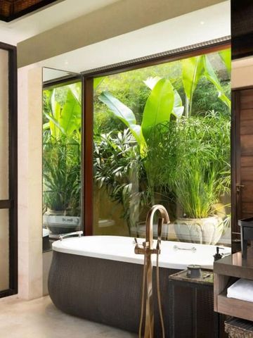 Luxuriöses Badezimmer mit großer Badewanne und Blick auf tropische Pflanzen im Mandapa Bali.