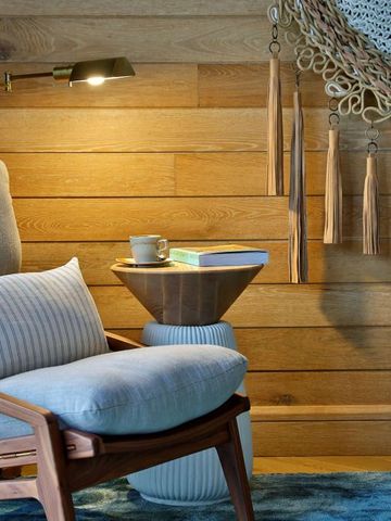 Gemütliche Leseecke mit Sessel, Beistelltisch und Lampe vor einer Holzwand.