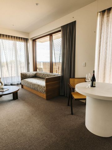 Hotelzimmer mit Sitzecke, rundem Tisch und bodentiefen Fenstern mit Vorhängen