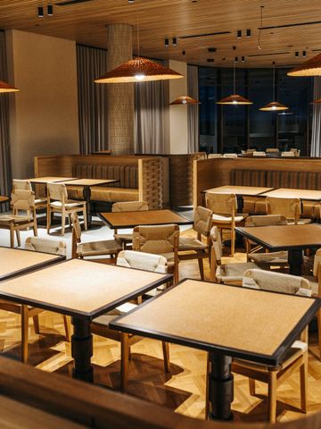 Restaurant mit Holztischen, Sitzbänken und Pendelleuchten vor großen Fenstern
