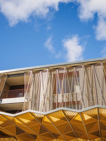 Fassade des Resorts mit Holzlamellen, Balkonen und gefaltetem Vordach unter blauem Himmel