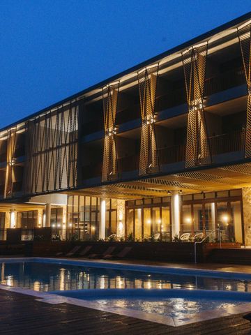 Beleuchtete Fassade des Resorts in der blauen Stunde, davor der Pool mit Liegen