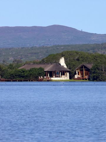 Blick auf Lodges am Ufer eines großen Gewässers mit Hügeln im Hintergrund