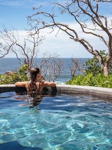 Frau entspannt im Infinity-Pool mit Blick auf den Ozean und exotischer Vegetation