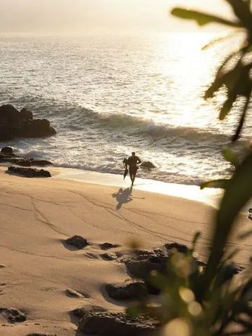 Person läuft am Sandstrand bei Sonnenuntergang entlang der Meeresküste