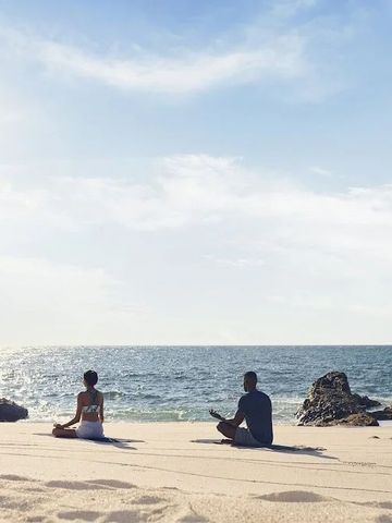 Zwei Personen meditieren am Sandstrand mit Blick auf das Meer