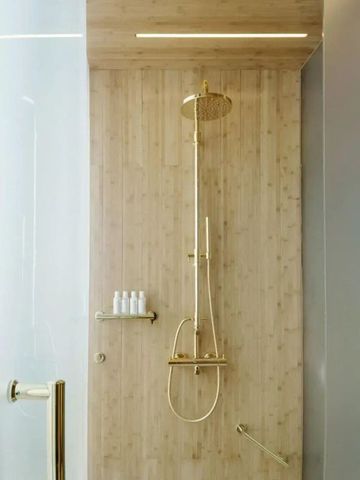 Edle Regendusche mit goldenen Armaturen vor Holzwand.