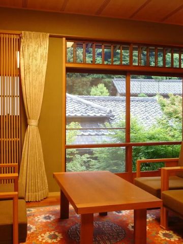 Gemütlicher japanischer Sitzbereich mit großen Fenstern und Blick auf traditionelle Dächer.
