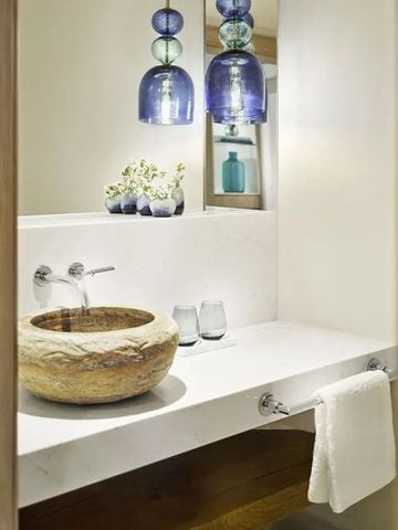 Modernes Badezimmer mit Natursteinwaschbecken und blauen Glaslampen.