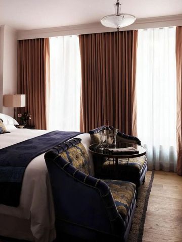 Luxuriöses Hotelzimmer mit großem Bett und Sesseln vor Vorhängen