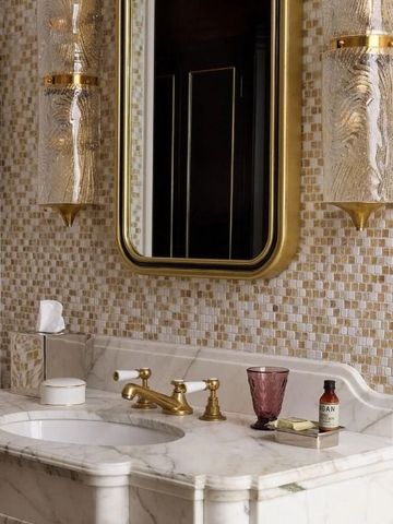 Marmordetails und goldene Armaturen im Badezimmer mit verspiegeltem Waschtisch.