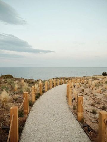Weißer Weg führt durch sandige Dünen zur ruhigen Küste mit Blick auf das Meer
