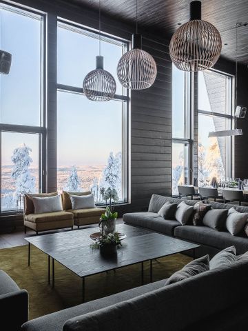 Lounge der Octola Lodge mit Kamin, großen Sofas und raumhohen Fenstern zum verschneiten Wald