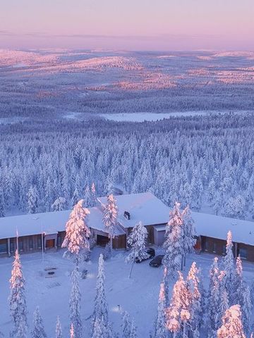 Luftbild der Octola Lodge zwischen verschneiten Bäumen, dahinter Fjells im rosa Morgenlicht