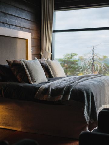 Schlafzimmer der Octola Lodge mit Doppelbett, Leselampe und Fenster zum Kiefernwald im Herbst
