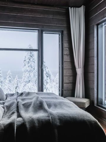 Schlafzimmer der Octola Lodge mit Doppelbett, Vorhängen und Fenstern zum verschneiten Wald