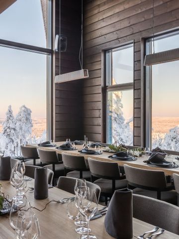 Lange gedeckte Tafel in der Octola Lodge vor Panoramafenstern mit Blick auf verschneite Bäume