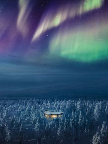 Nordlichter über dem Wald, darunter die beleuchtete Octola Villa in der verschneiten Landschaft