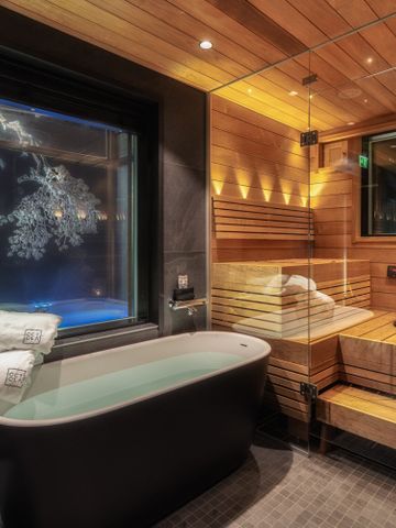Bad der Octola Villa mit freistehender Wanne und verglaster Sauna, Fenster zur Winternacht