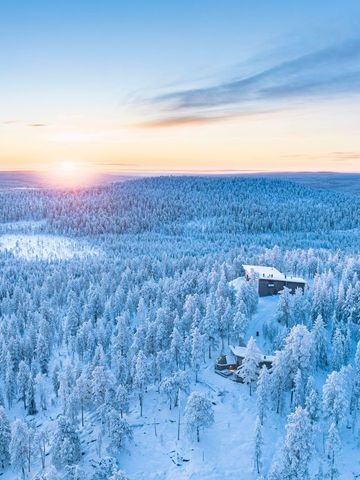 Luftbild der verschneiten Wildnis bei Sonnenaufgang mit einem einzelnen Gebäude im Wald