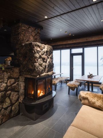 Karhu-Bar mit Steinkamin, Fellsitzen und Holztischen vor großen Fenstern