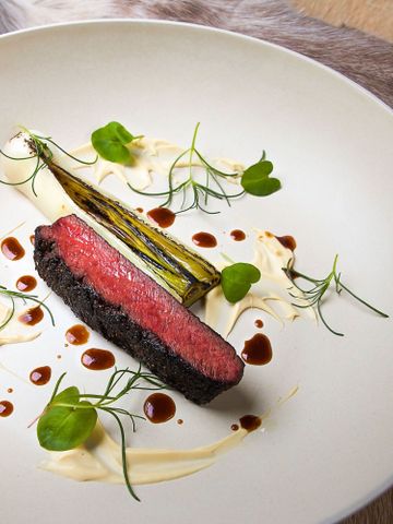Rentierfilet mit Spargel, Kräutern und Sauce auf weißem Teller, darunter ein Fell