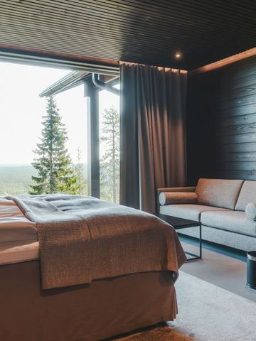 Schlafzimmer der Ultra Lodge mit Doppelbett, Sitzecke und Fenster zum Kiefernwald