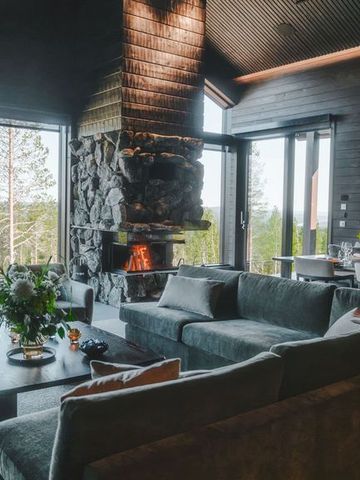 Wohn- und Essbereich der Villa mit Steinkamin, Sofas und Fenstern zum Kiefernwald