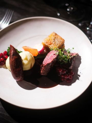 Wildgericht mit Beeren und Gemüse auf weißem Teller auf dunklem Holztisch