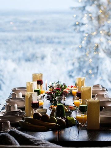 Gedeckter Frühstückstisch mit Kerzen und Blumen vor einem Fenster zur Schneelandschaft