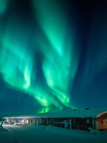 Grüne Nordlichter über der verschneiten Aurora Radar Station auf dem Fjell