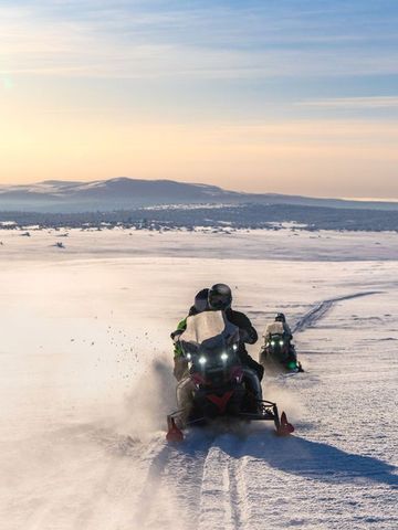 Zwei Schneemobile fahren über das verschneite Fjell im Licht der tiefstehenden Sonne