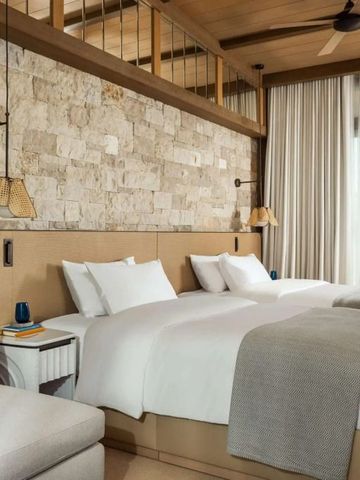 Helles Hotelzimmer mit rustikaler Steinwand und zwei komfortablen Betten