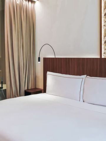 Helles Hotelzimmer mit großem Bett und dezenter Beleuchtung.