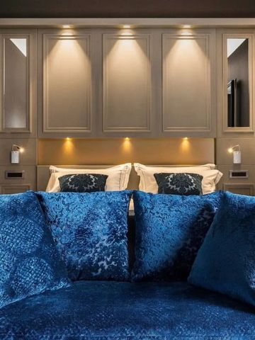 Elegante Bettrückwand mit blauen Kissen und warmer Beleuchtung.