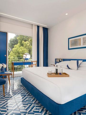 Hotelzimmer mit Balkon, blau-weißen Akzenten und grüner Aussicht