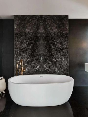 Luxuriöse Badezimmer mit freistehender Badewanne und schwarzem Marmor-Wanddekor.