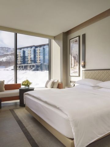 Helles Hotelzimmer mit großem Bett und Winterlandschaft im Hintergrund.