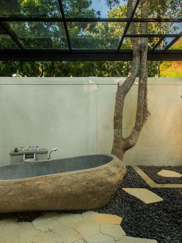 Outdoor-Badezimmer mit Steinbadewanne und Bäumen, natürliche Umgebung.