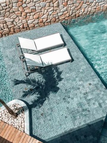 Sonnenliegen am Pool mit Schatten einer Palme, umgeben von Steinmauer.