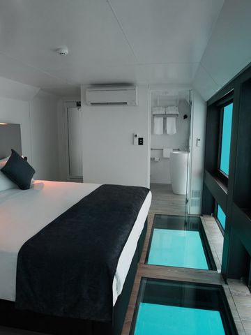 Reefsuite mit Doppelbett vor Unterwasserfenstern, Fische ziehen vorbei, Glasboden vor dem Bett