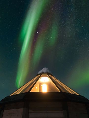 Beleuchtete Glaskuppel eines Iglus unter grünen Nordlichtern am Nachthimmel