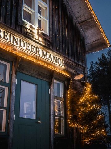 Eingang des historischen Holzhauses mit Schild Reindeer Manor und Lichterketten bei Nacht