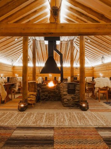 Kammi-Hütte aus Holz mit offener Feuerstelle, gedeckten Tischen, Fellen und Laternen