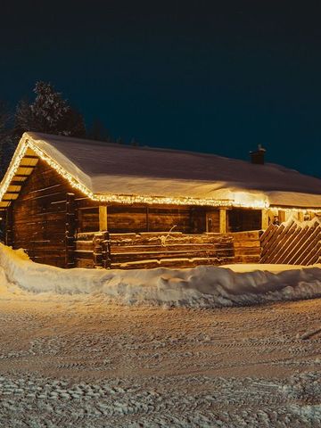 Altes Saunahaus aus Holz mit Lichterketten am Dach in einer verschneiten Winternacht